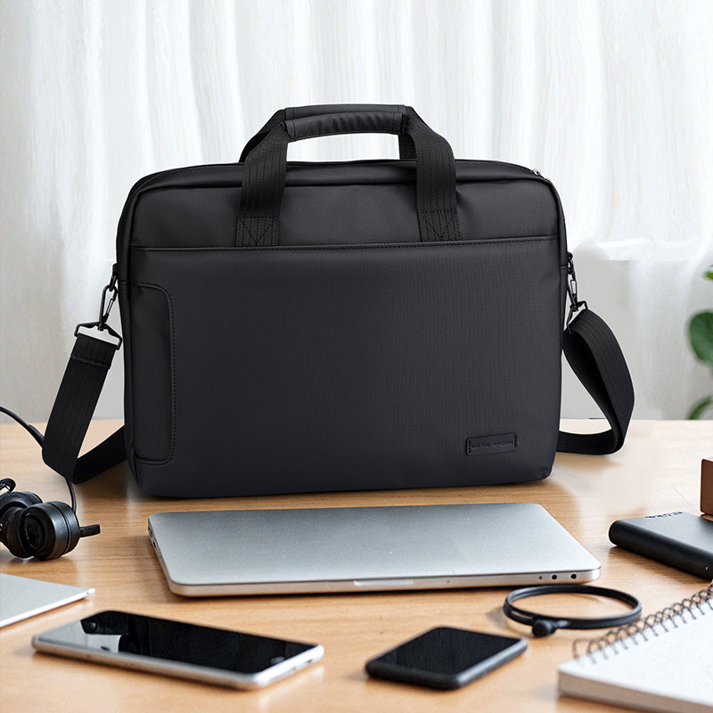 Black MarkRyden Tech Commuter Computer Briefcase 14/15.6 inch with dual handles and shoulder strap, displayed on a wooden desk with laptop, smartphones, and tech accessories.
