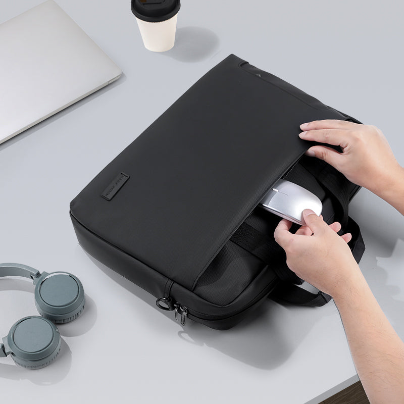 Black MarkRyden Classic IV Tech Commuter Computer Briefcase 14/15.6 inch with hands placing a mouse into a front pocket, surrounded by headphones and a laptop on a desk.