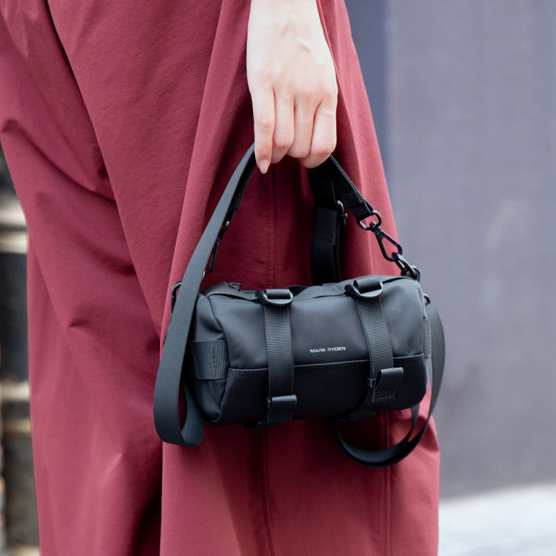 Hand holding Mark Ryden black cylinder crossbody bag with strap