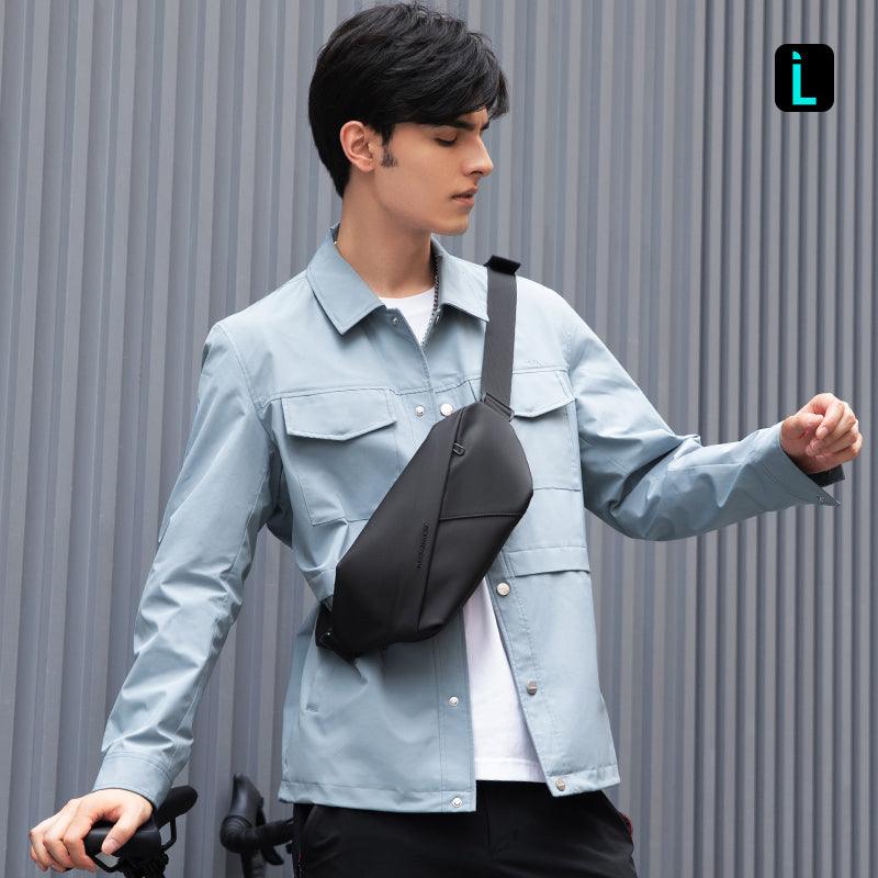 UrbanStride compact city explorer satchel crossbody bag in black, worn by man in light blue jacket