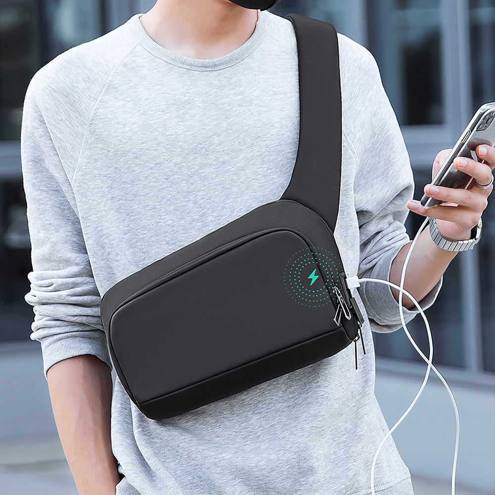 Mark Ryden Global's Breck Daily waterproof black crossbody bag with wireless charging feature worn by model in gray sweatshirt