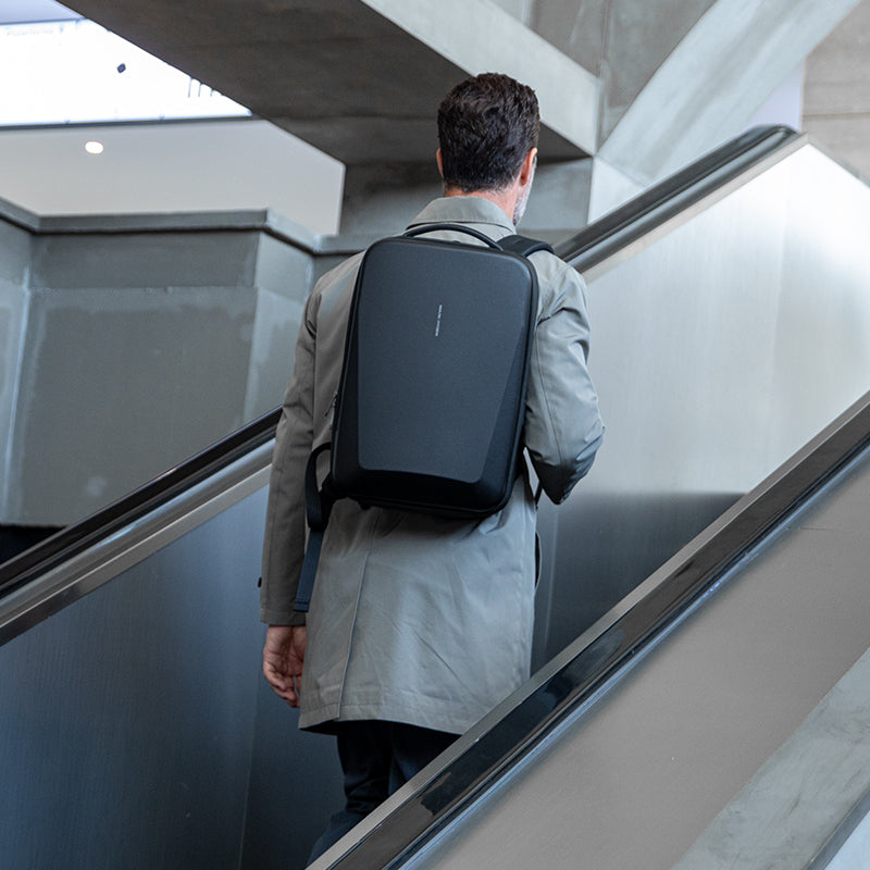 Man wearing gray coat carries black Mark Ryden hard-shell backpack on escalator