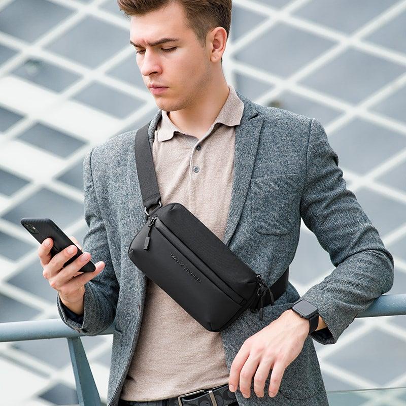 Mark Ryden Global: Man in gray blazer wears lightweight waterproof crossbody bag with multiple compartments