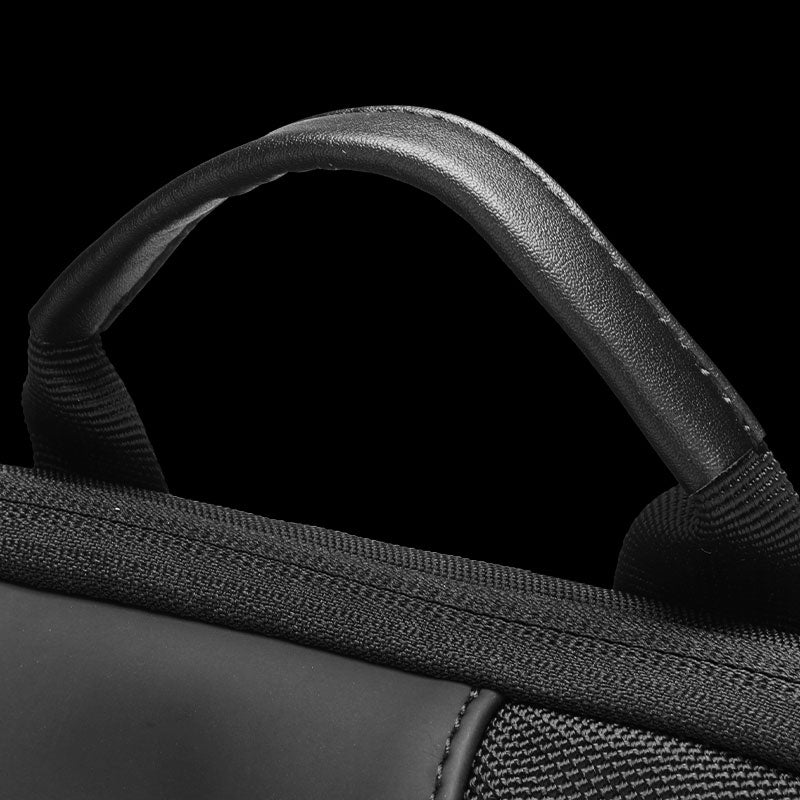 Close-up of black leather-like backpack handle with padded grip, attached to water-repellent fabric with visible stitching.